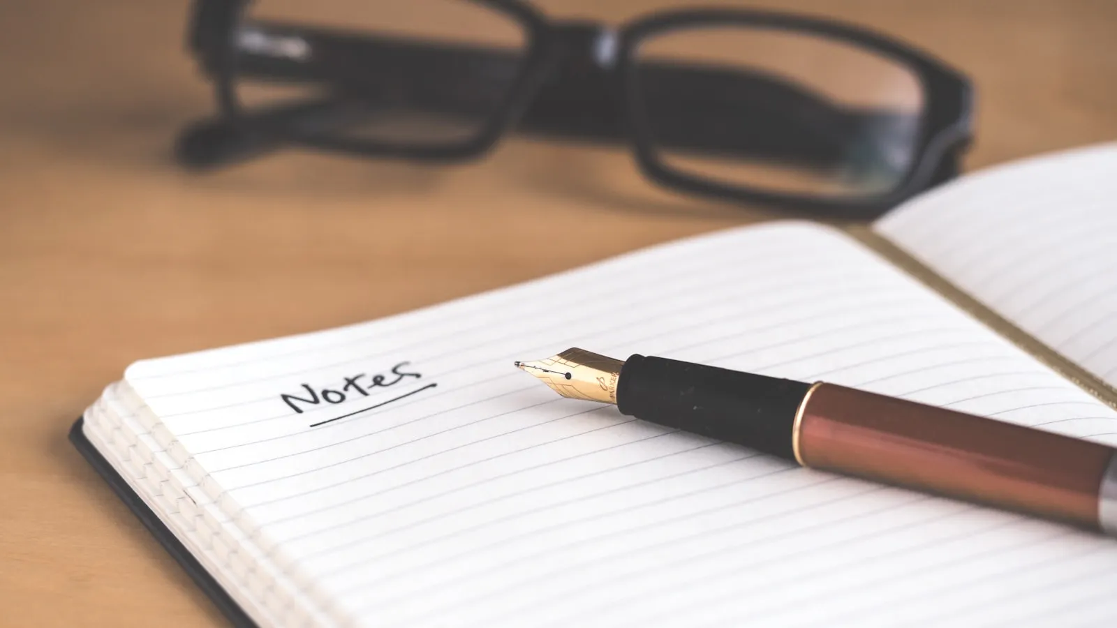 Notebook and pen on a wooden desk, a coffee cup beside them